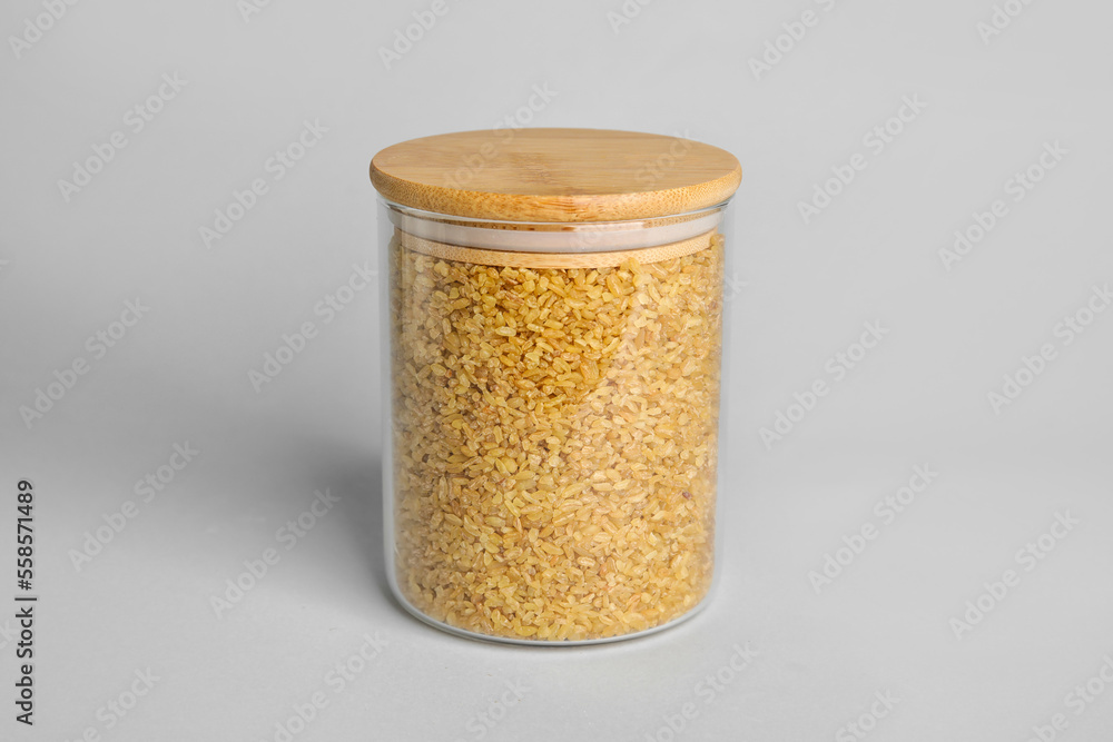 Glass jar of bulgur on white background