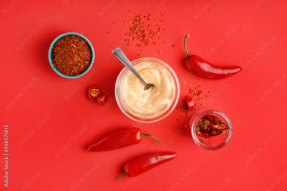 Glass of tasty chipotle sauce and spices on red background