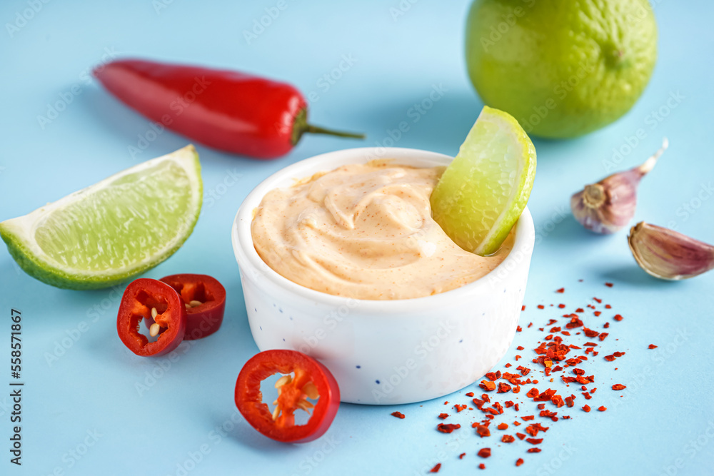 Bowl of tasty chipotle sauce with lime on color background