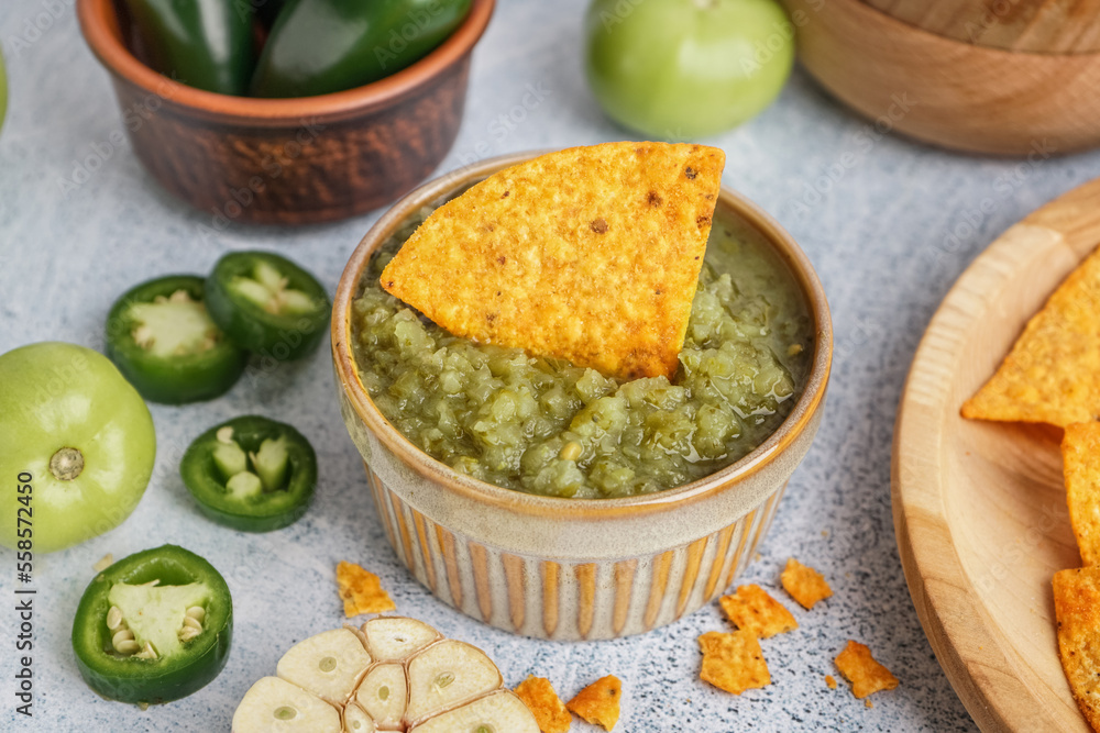 Bowl of tasty green salsa sauce with nacho on light background