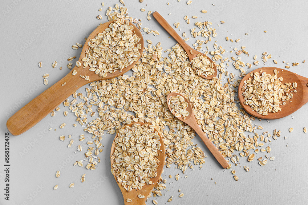 Different spoons with raw oatmeal on grey background