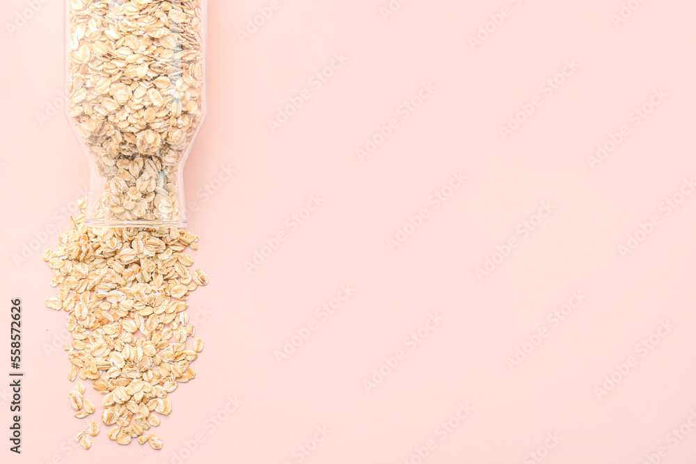 Overturned bottle of raw oatmeal on pink background