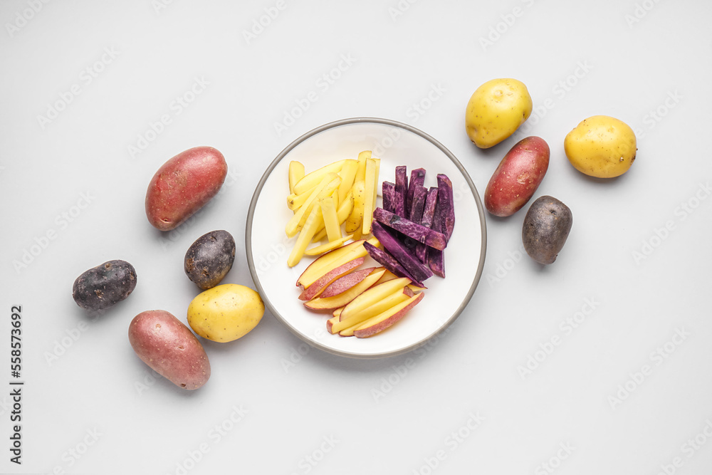 Plate with cut and whole raw potatoes on light background