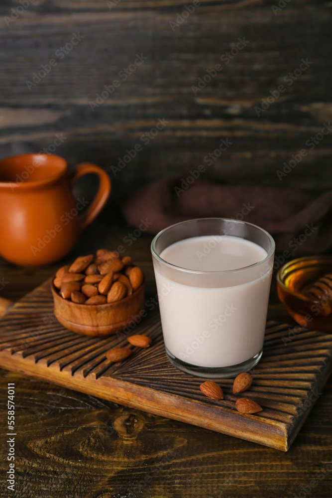 Cutting board with glass of almond milk and nuts on wooden table, closeup