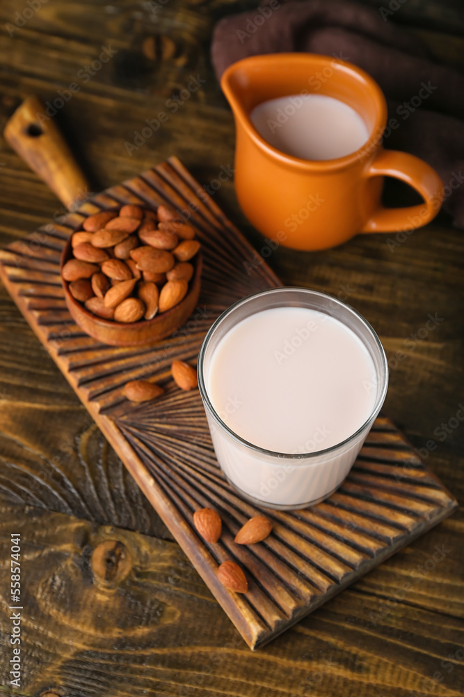 Cutting board with glass of healthy almond milk and nuts on wooden background