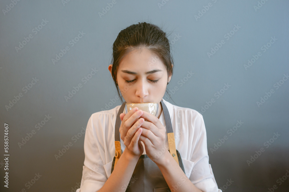 Portrait of beautiful young barista Asian woman drinking coffee milk foam on isolated gray backgroun