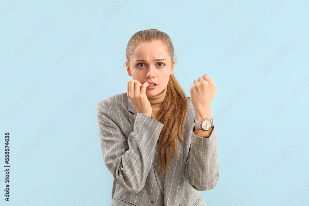 Young businesswoman with wristwatch biting nails on blue background