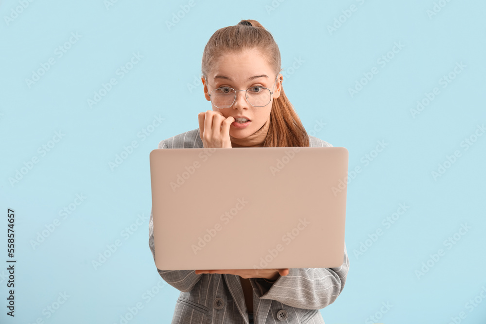 Young businesswoman with laptop biting nails on blue background