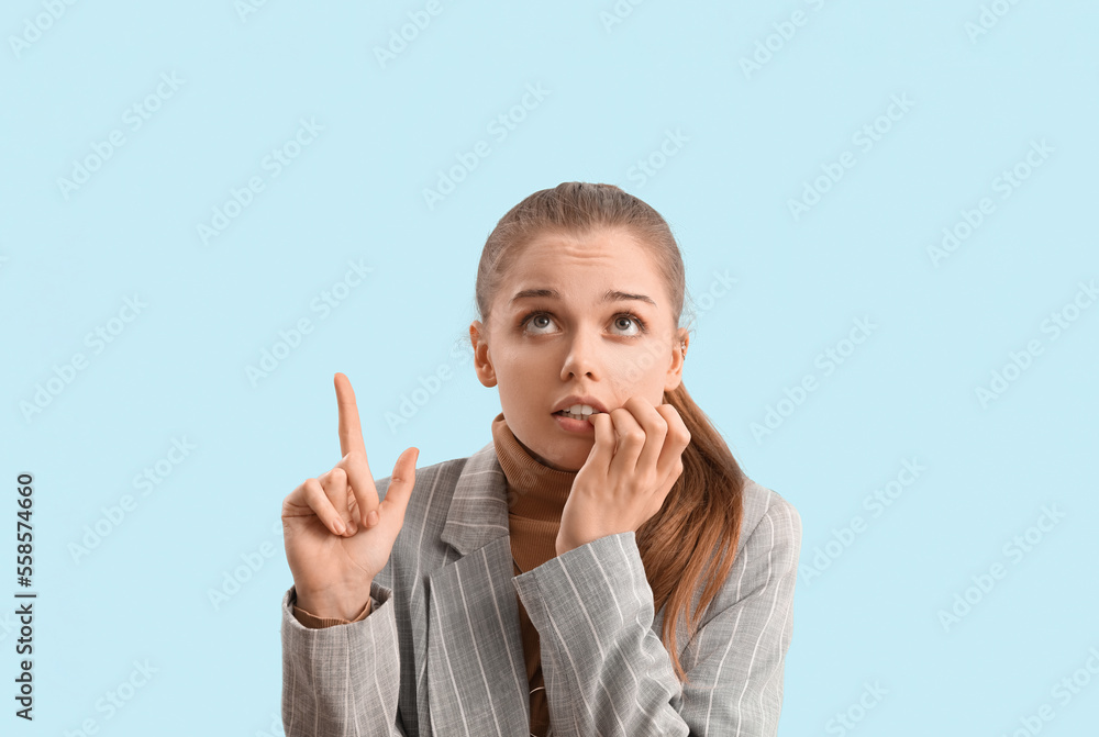 Young businesswoman biting nails and pointing at something on blue background