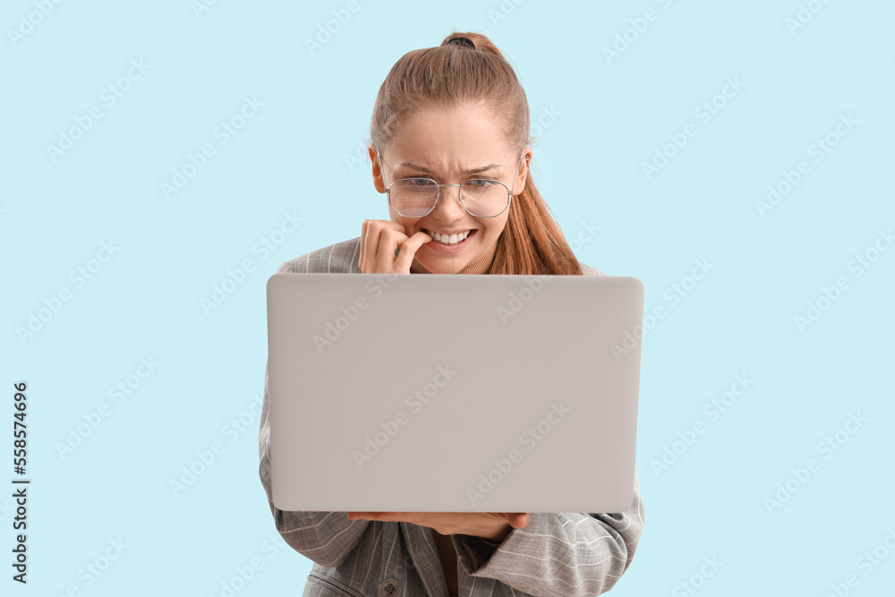 Young businesswoman with laptop biting nails on blue background