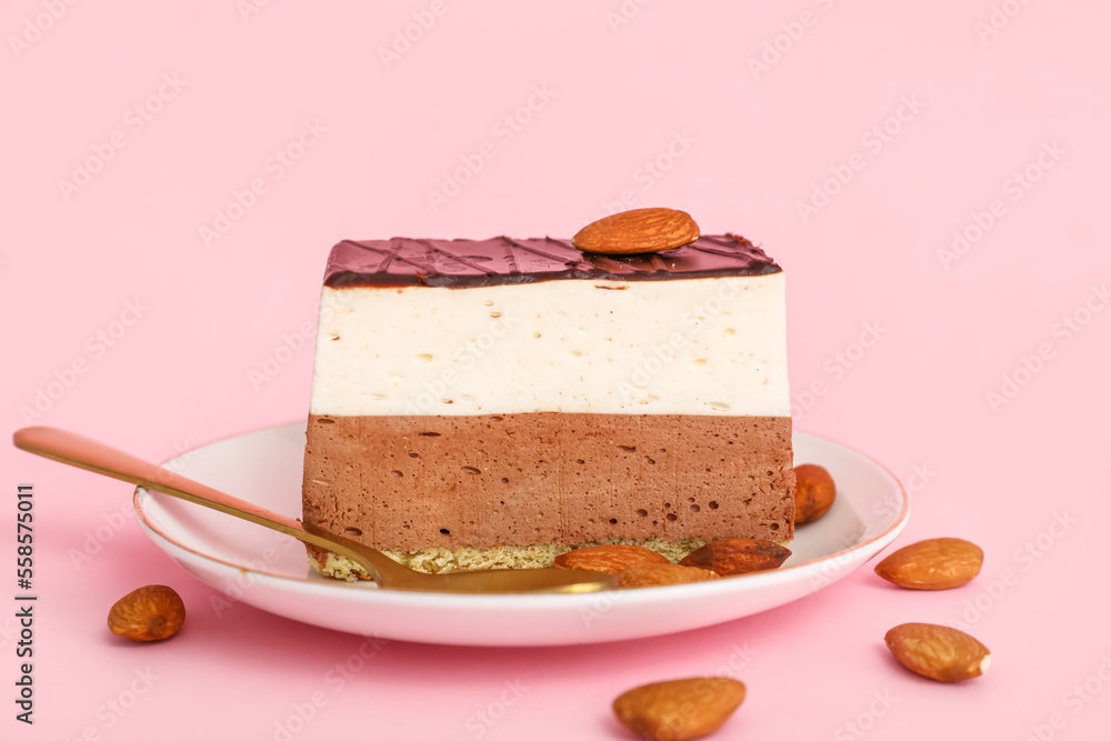 Plate with piece of birds milk cake, almond nuts and spoon on pink background