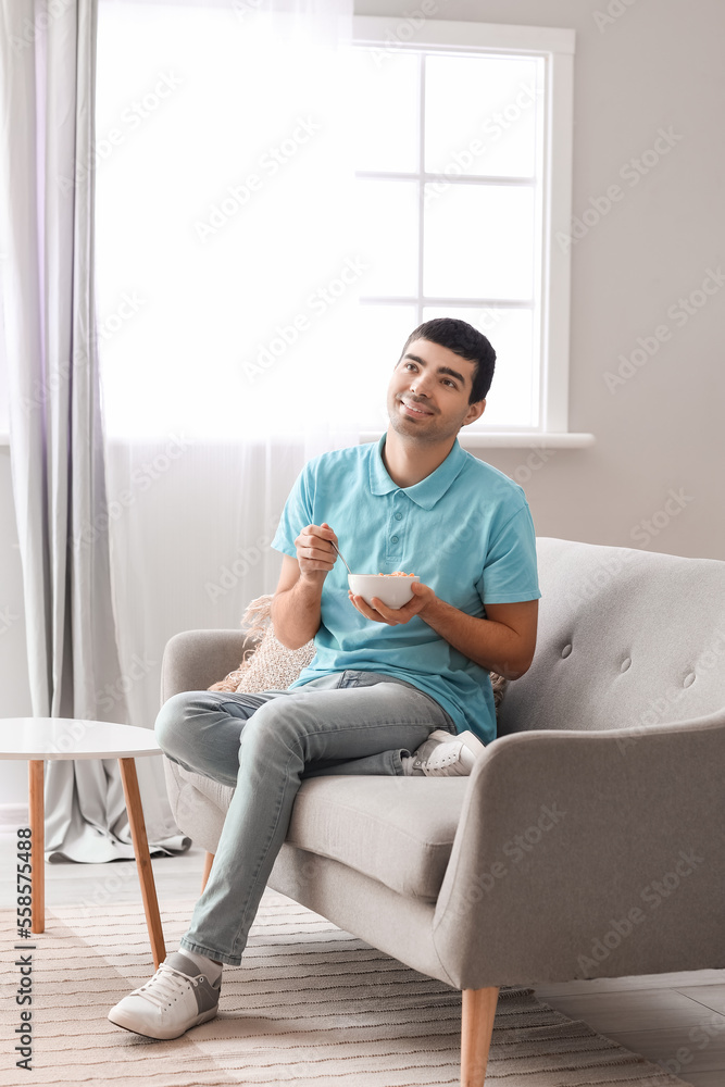 Young man eating cornflakes with spoon at home