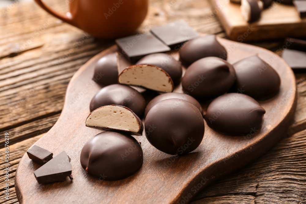 Cutting board with sweet chocolate birds milk candies on wooden background, closeup