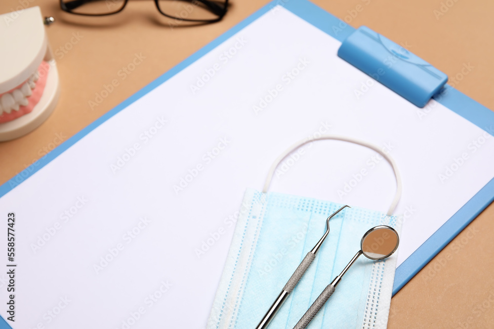 Clipboard with medical mask and dental tools on brown background, closeup