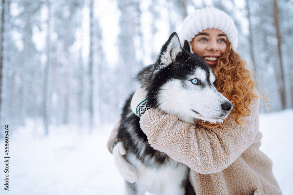 Happy woman walking her dog in the winter and both explore the snow together in playful mood. Friend