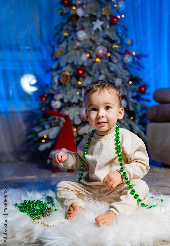 Cute child with christmas tree. Happy baby sitting near a fir tree and holding a christmas ornament 