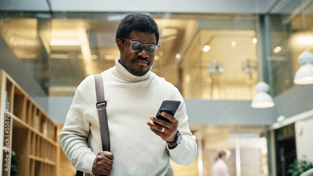 Portrait of a Black Man Walking in Corporate Office while Scrolling on his Smartphone. A Businessman