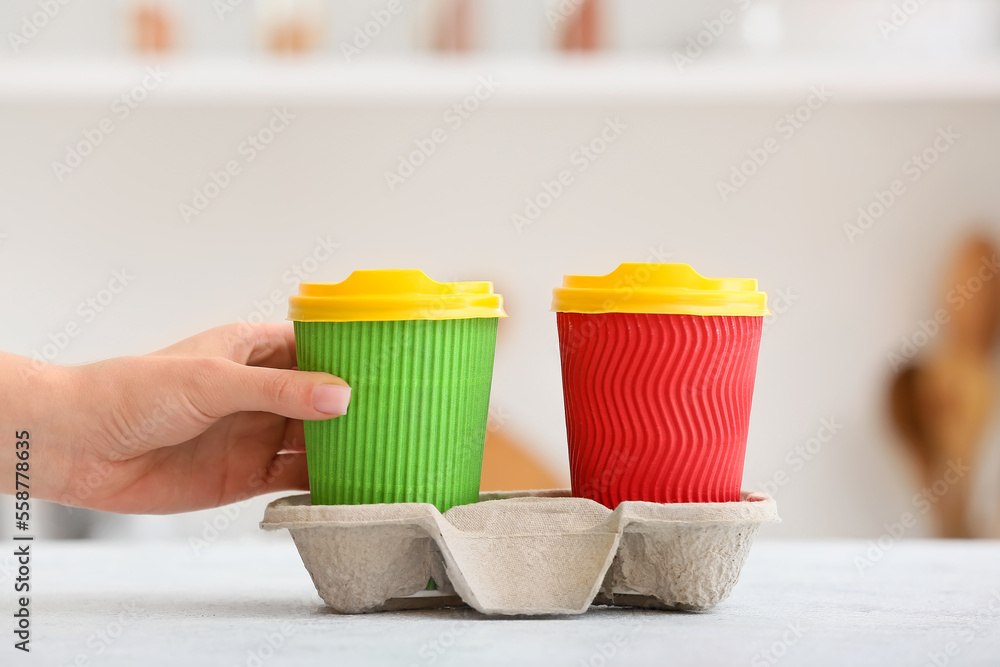 Woman taking paper cup with drink from holder on table