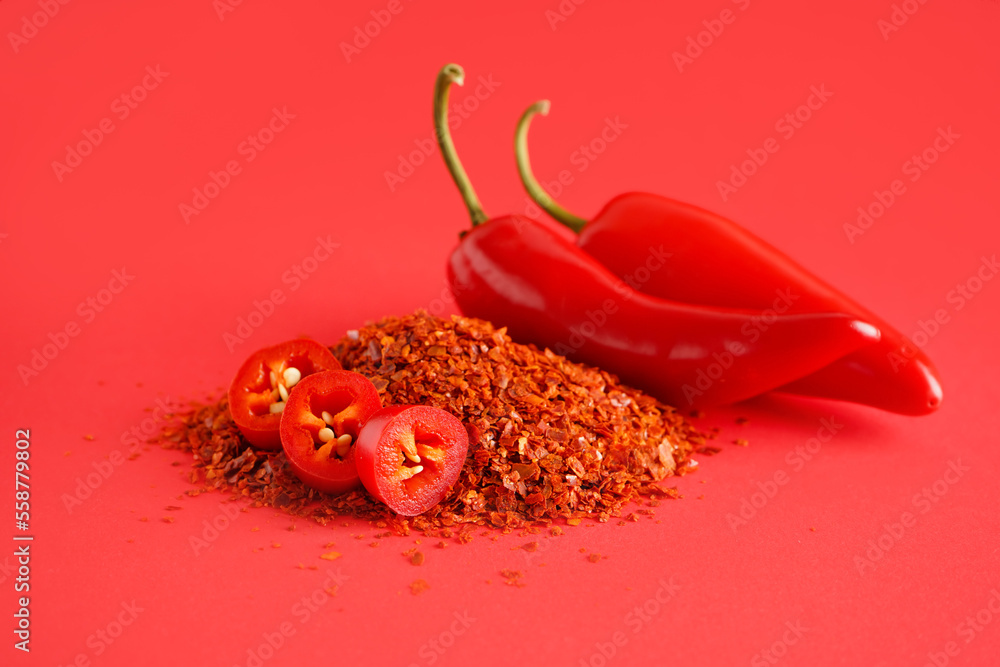 Heap of chipotle chili flakes and fresh jalapeno peppers on red background