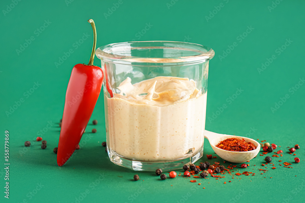 Glass of tasty chipotle sauce on green background