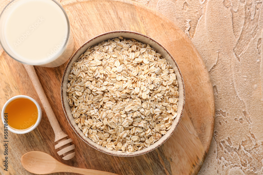 Wooden board with bowl of raw oatmeal, honey and milk on color background, closeup