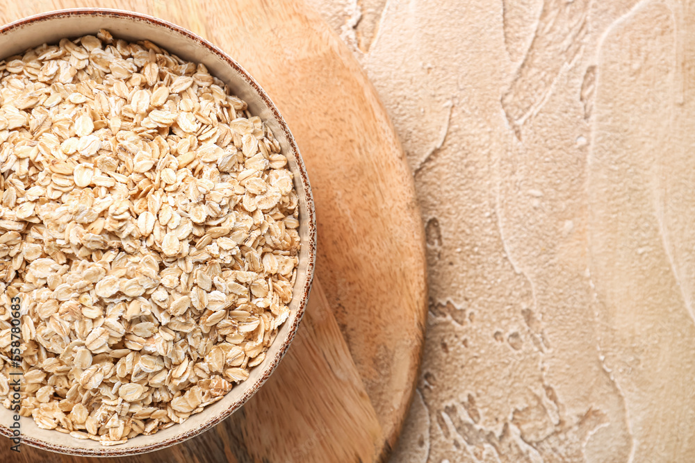 Wooden board with bowl of raw oatmeal on color background, closeup