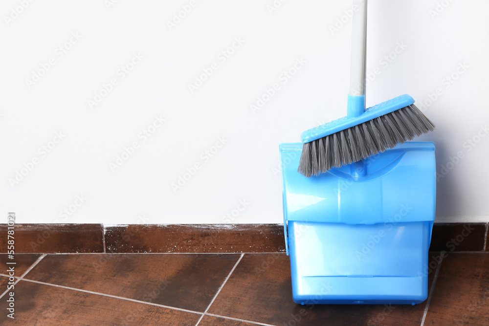 Dustpan and broom on tile floor near white wall