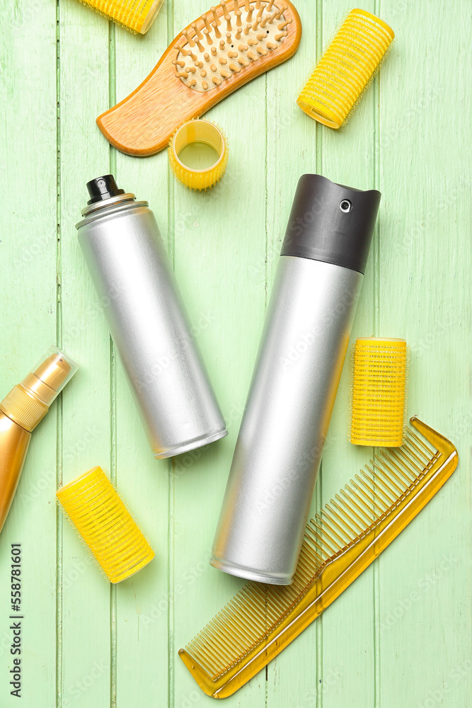 Hair sprays with curlers and combs on green wooden background