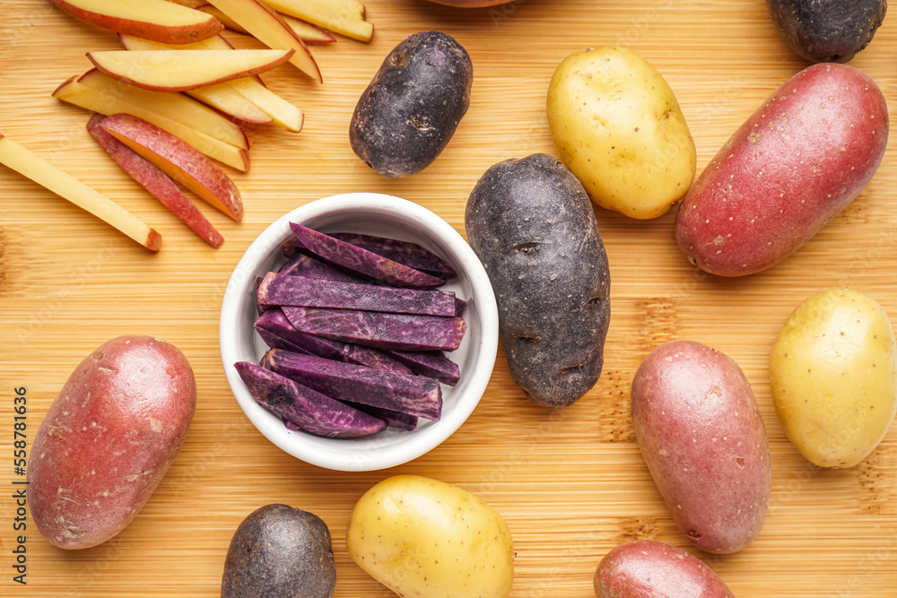 Wooden board with different raw potatoes, closeup