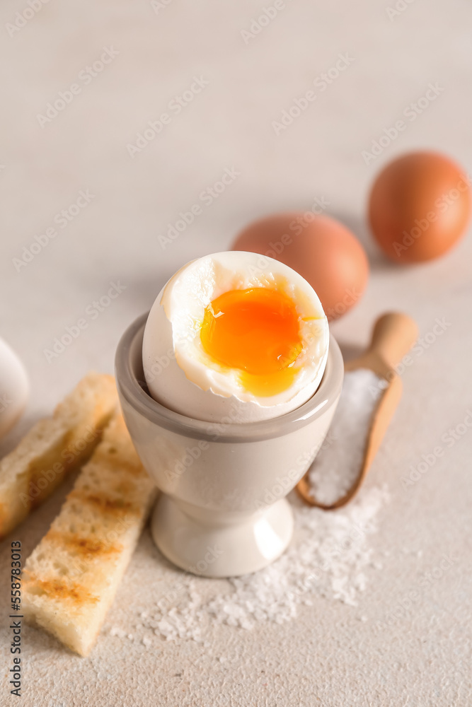 Holder with soft boiled egg, toasted bread and scoop on white table