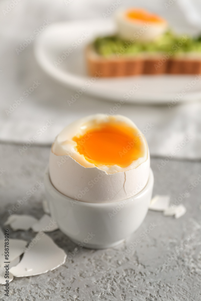 Holder with soft boiled egg and shell on grey table