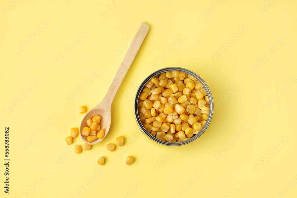 Tin can and spoon with corn kernels on yellow background