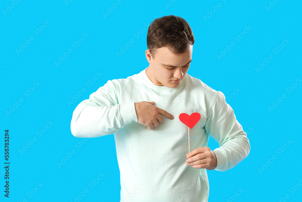 Young man pointing at paper heart for Valentines Day on blue background