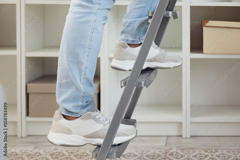 Young man on ladder near bookshelf at home, closeup