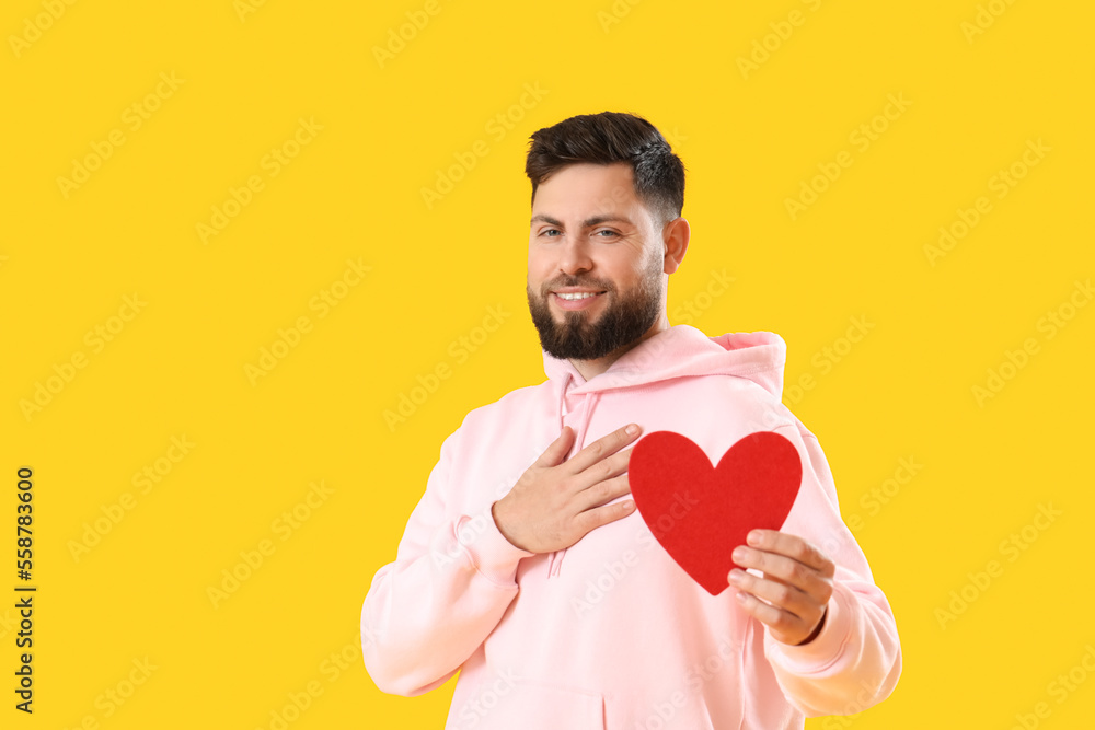 Young bearded man with paper heart for Valentines Day on yellow background