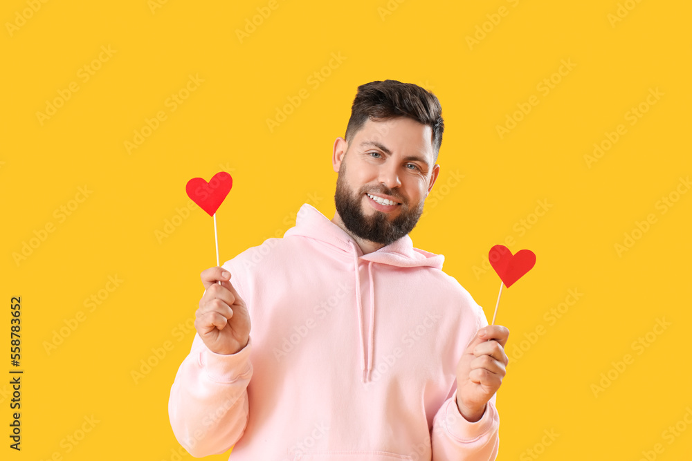 Young bearded man with paper hearts for Valentines Day on yellow background