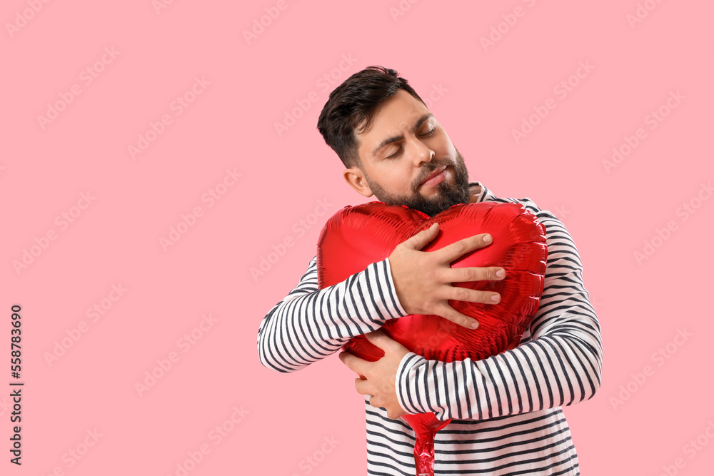 Young bearded man hugging balloon for Valentines Day on pink background