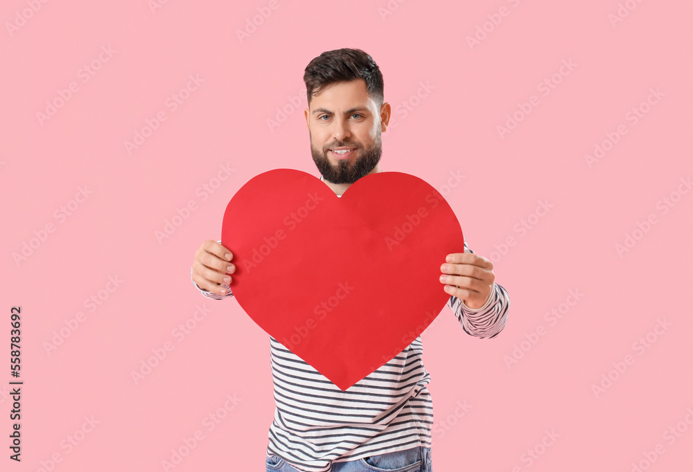 Young bearded man with big paper heart for Valentines Day on pink background