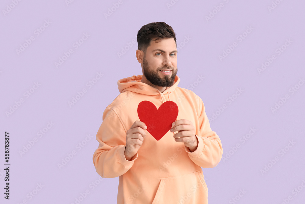 Young bearded man with paper heart for Valentines Day on lilac background