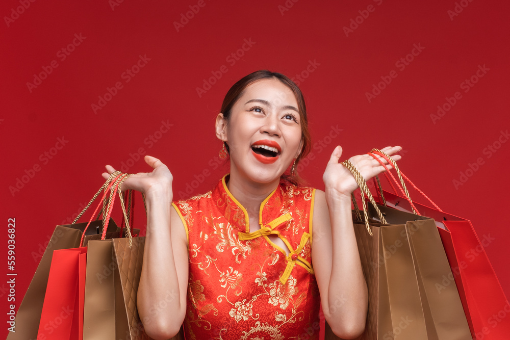 Young asian woman wearing qipao cheongsam dress with shopping bags on red background for Chinese new