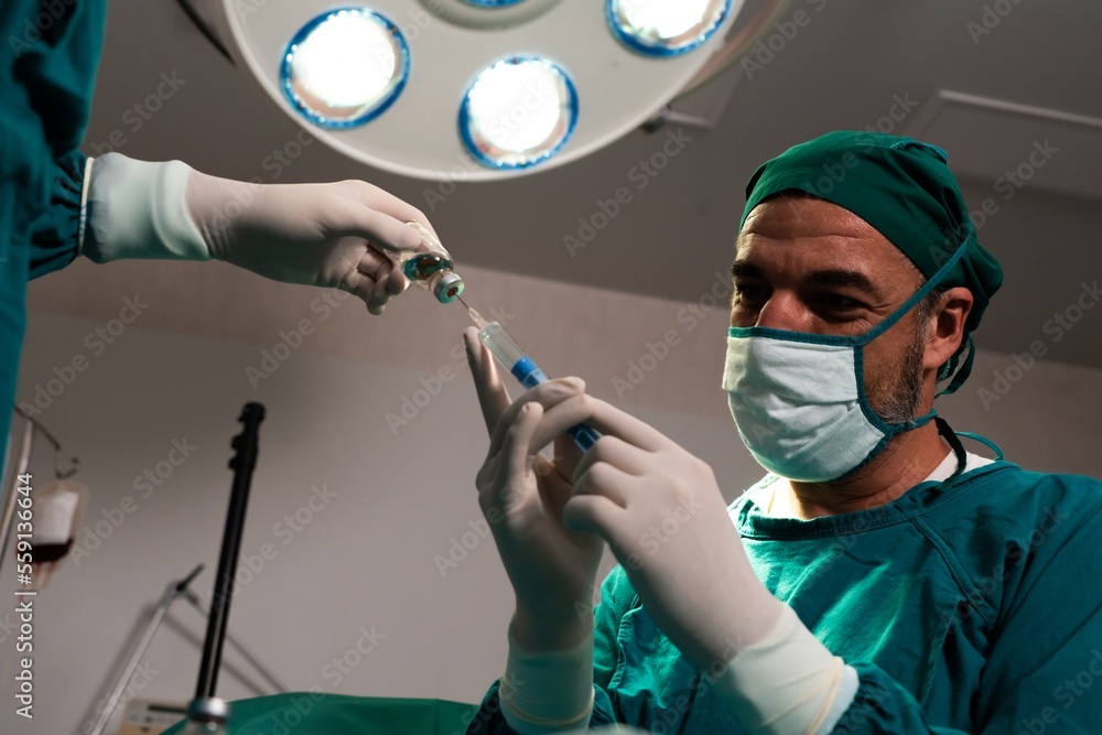 Surgeon fill syringe from medical vial for surgical procedure at sterile operation room with assista