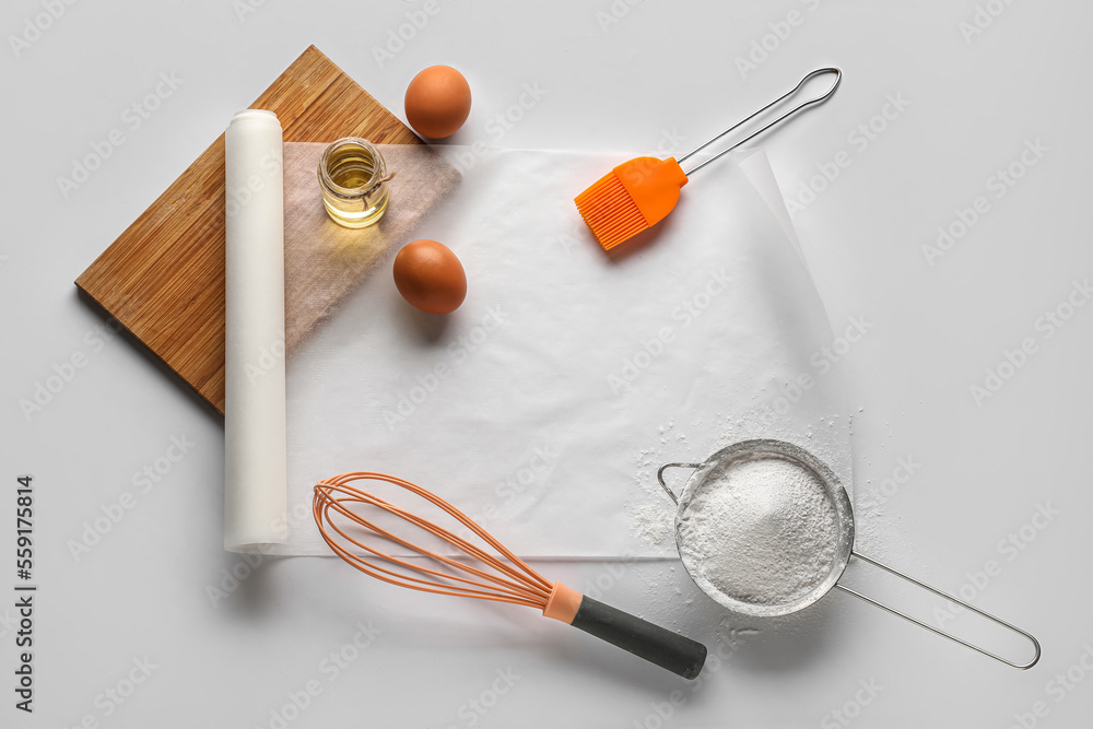 Baking paper with kitchen supplies and ingredients on white background