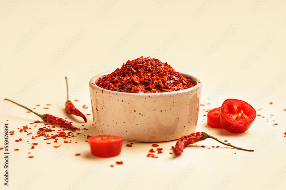 Bowl of chipotle chili flakes on color background