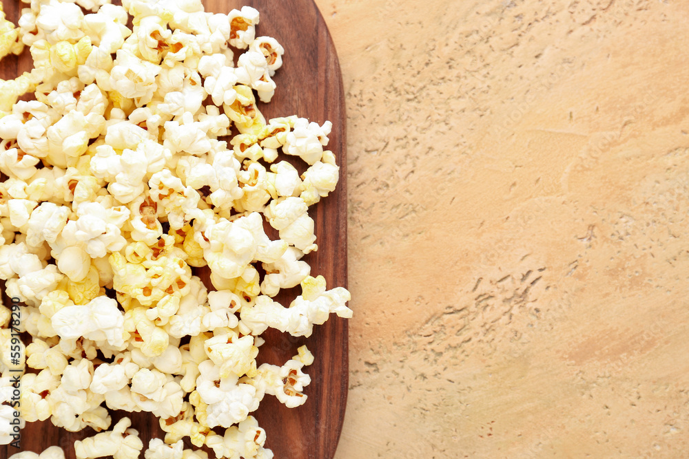 Wooden board with tasty popcorn on color background, closeup