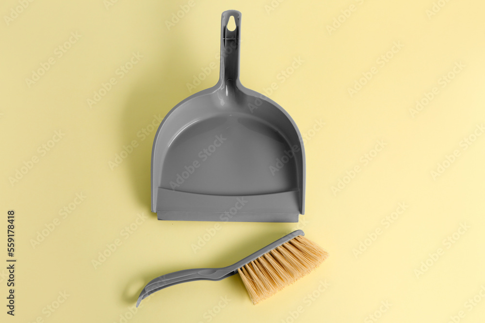 Dustpan and cleaning brush on yellow background