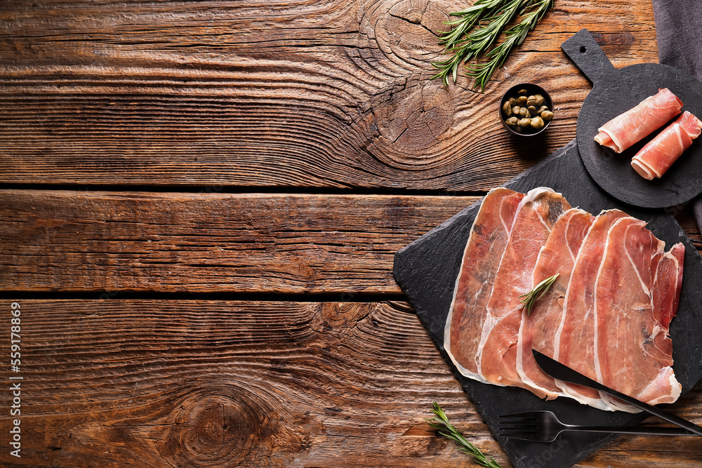 Slate boards with slices of tasty ham and capers on wooden background