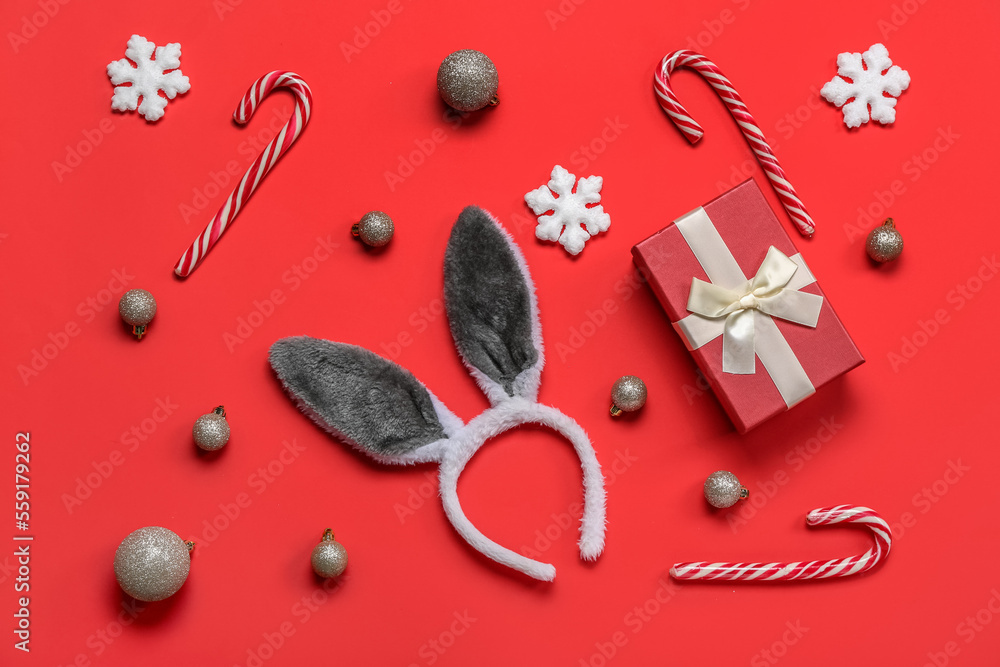 Bunny ears with Christmas balls, gift and candy canes on red background