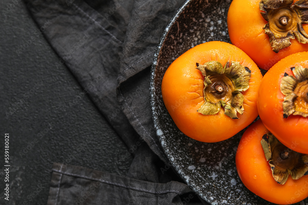 Plate with fresh ripe persimmons on dark background