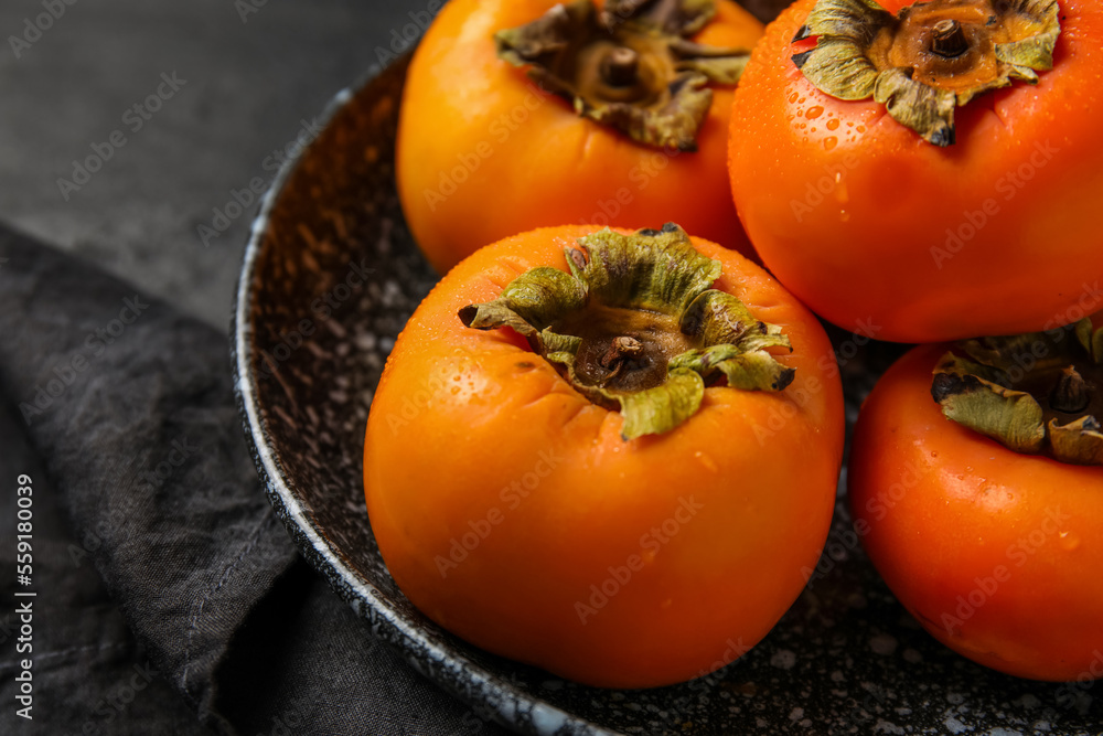 Plate with fresh ripe persimmons on dark background, closeup