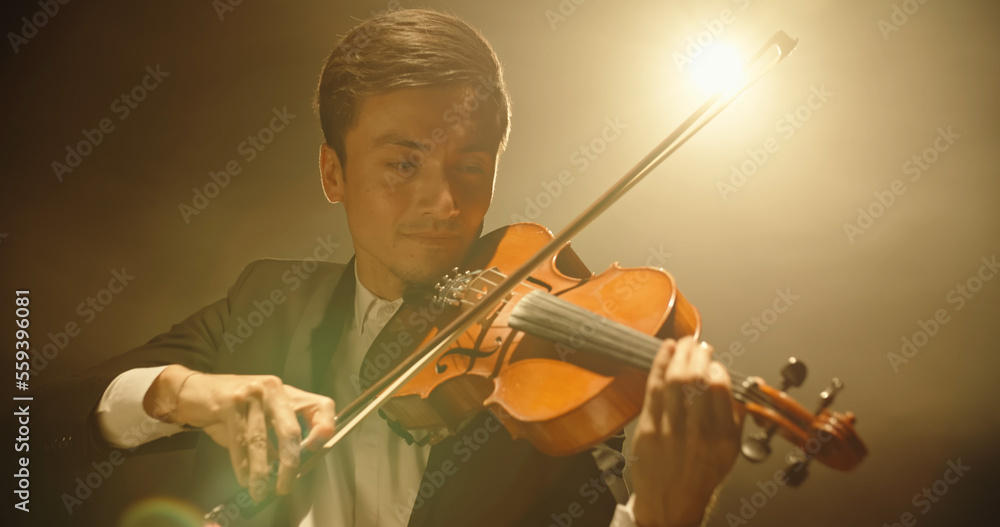 Experienced Violinist performing amazing solo on stage, spotted by light on black background close u